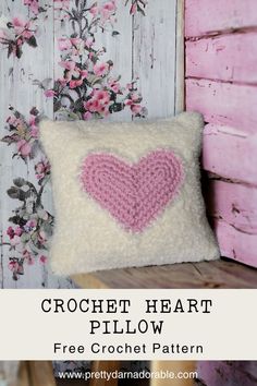 a crochet heart pillow on a wooden bench with pink flowers in the background