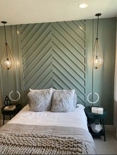 a bed with two lamps hanging from the ceiling and pillows on it's headboard