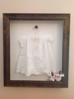 a baby's white shirt and shoes are in a shadow box on the wall