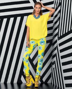 a woman standing in front of a black and white wall wearing bright yellow pants with blue flowers on them