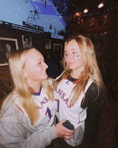 two young women standing next to each other in front of a flat screen tv on a wall