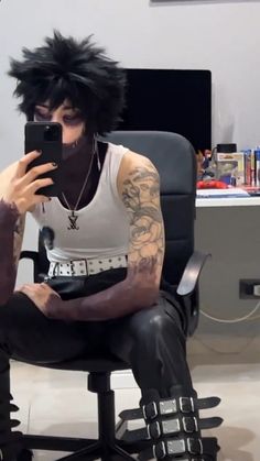 a man with black hair sitting in a chair holding a cell phone