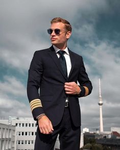 a man in a suit and sunglasses standing on the roof of a building with his hands in his pockets