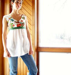 a woman standing in front of a window wearing jeans and a white top with flowers on it