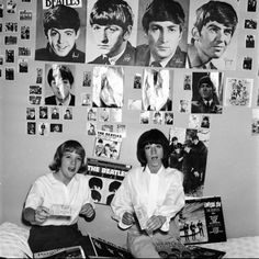 black and white photo of two women sitting on a bed in front of beatles posters