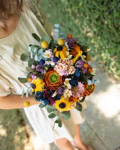 a woman holding a bouquet of colorful flowers in her hands and looking down at the ground