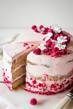 a cake with pink frosting and raspberries on top is cut in half