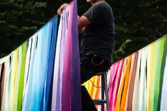 a man standing on a ladder next to rainbow colored streamers