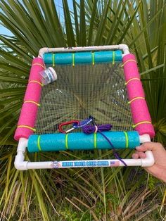 a person holding up a pink and blue net with scissors on it in front of some palm trees