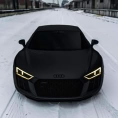 the front end of a black sports car with gold headlights on snow covered road in winter