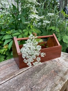 a wooden box with white flowers in it sitting on a table next to some plants