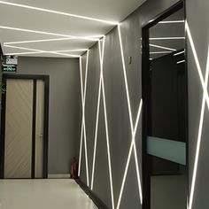 an empty hallway with lights on the ceiling and doors in the center, leading to another room