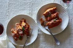 two white plates topped with lasagna covered in sauce next to glasses of wine