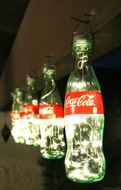 coca - cola bottles are hanging from the ceiling with string lights in front of them