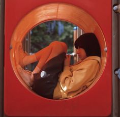 a woman laying down in a red and orange play structure with her feet on the ground