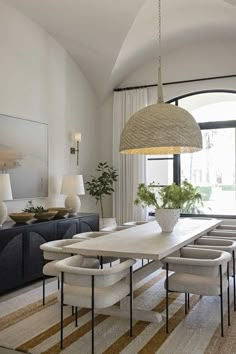 a dining room table with white chairs and an oval chandelier hanging from the ceiling