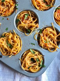 several muffin tins filled with spaghetti and sauce on top of a blue cloth