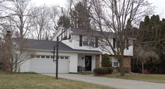 a large white house with two garages and trees in the front yard on a cloudy day