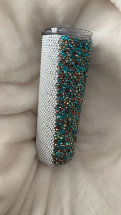 a white cup with blue and gold sequins on it sitting on a blanket