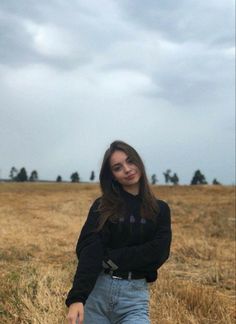 a woman standing in a field with her arms crossed and looking off to the side