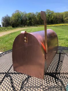 a large metal mailbox sitting on top of a table in front of a field