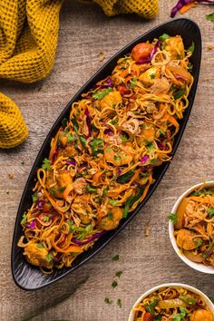 two bowls filled with noodles and vegetables on top of a wooden table next to a yellow blanket