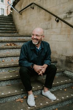 a man sitting on some steps with his hands clasped in front of him and smiling at the camera