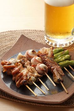 a plate with meat and vegetables on skewers next to a glass of beer