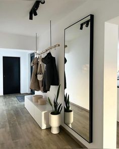 an empty room with clothes hanging on the rack and potted plants next to it