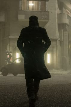 a man is walking down the street in the snow at night with his back turned to the camera