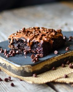 a piece of chocolate cake sitting on top of a wooden table covered in chocolate chips