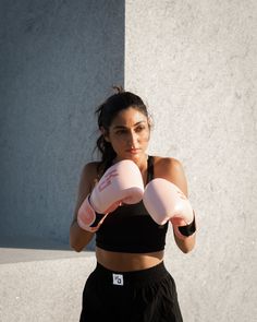 a woman wearing pink boxing gloves standing in front of a wall with her hands on her hips