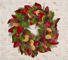 a christmas wreath with pine cones, poinsettis and berries on a brick wall