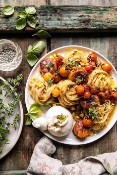 a white plate topped with pasta and tomatoes next to an egg on a wooden table