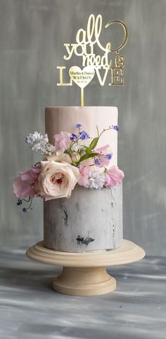 a white and pink cake with flowers on top that says all you need is love