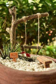 a miniature garden is in a pot with rocks and plants on the ground, along with a wooden bench