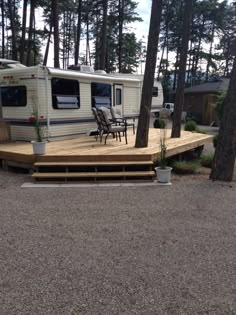 an rv parked on top of a wooden deck in the woods next to a picnic table and chairs