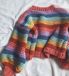 a multicolored sweater laying on top of a white bed next to a pillow