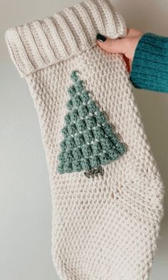 someone is holding up a knitted christmas stocking with a tree on the bottom