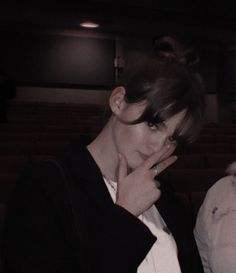 a woman is holding her hand up to her face while sitting in a theater seat