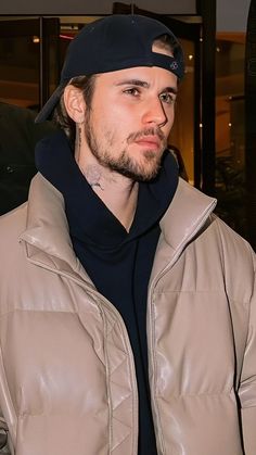 a man wearing a beanie and jacket looks off to the side while standing in front of a building