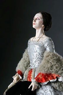 a woman in a silver dress and fur stoler holding a black hat with red trim