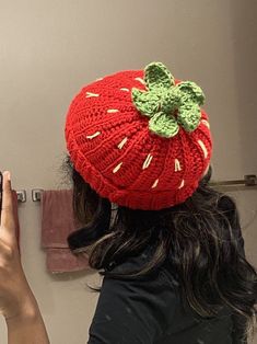 a woman wearing a red knitted strawberry hat taking a selfie with her cell phone