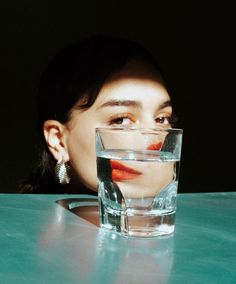 a woman sitting at a table with a glass of water in front of her face