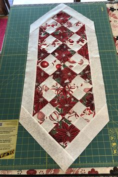 a quilted table runner with red and white flowers on it, sitting on top of a green cutting board