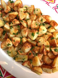 a white plate topped with potatoes and parsley on top of a red table cloth