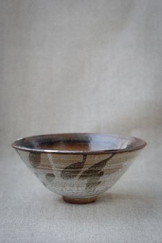 a brown and white bowl sitting on top of a beige cloth covered table next to a wall