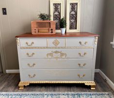 an old dresser has been painted with gold and white paint, along with two framed pictures on the wall