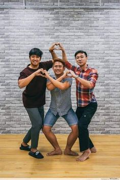 three men standing in front of a brick wall making the shape of a heart with their hands