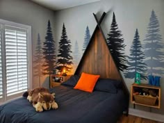 a child's bedroom decorated in blue and gray with trees painted on the wall